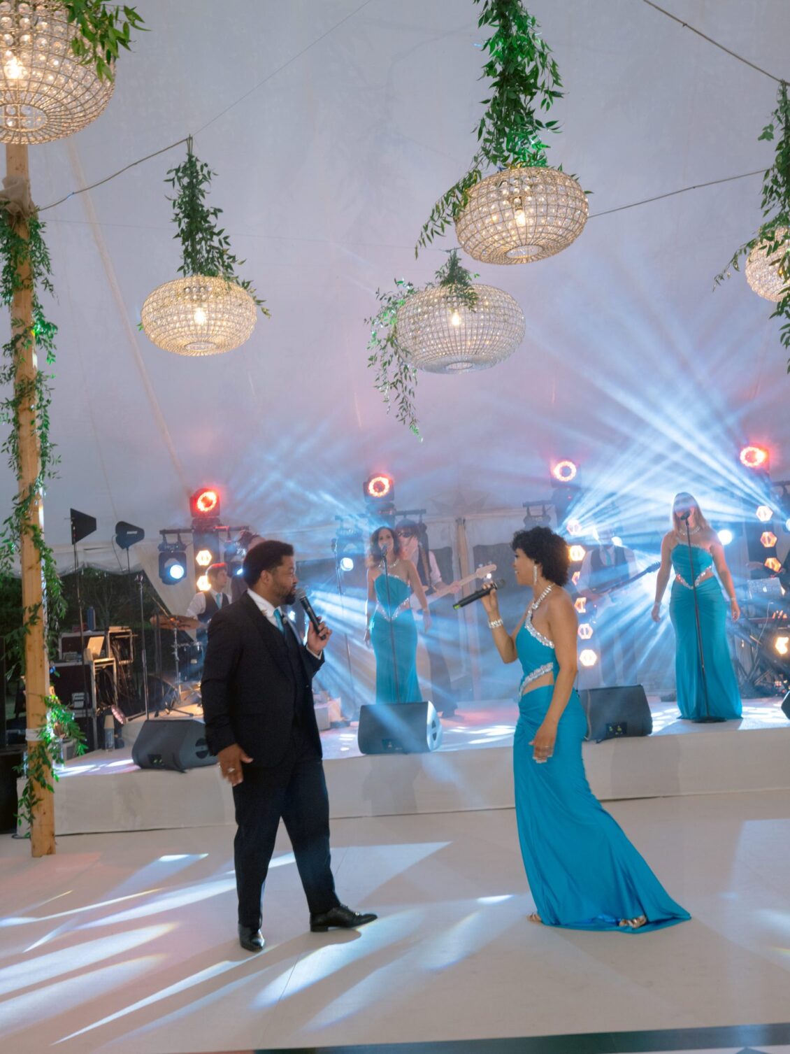Two singers perform a duet on the dance floor beneath hanging greenery and chandeliers