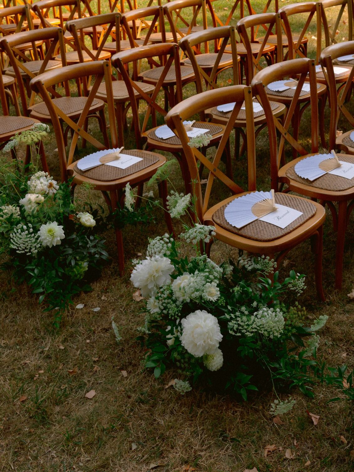 Wooden ceremony chairs set with programmes, with white hydrangea arrangements along the aisle