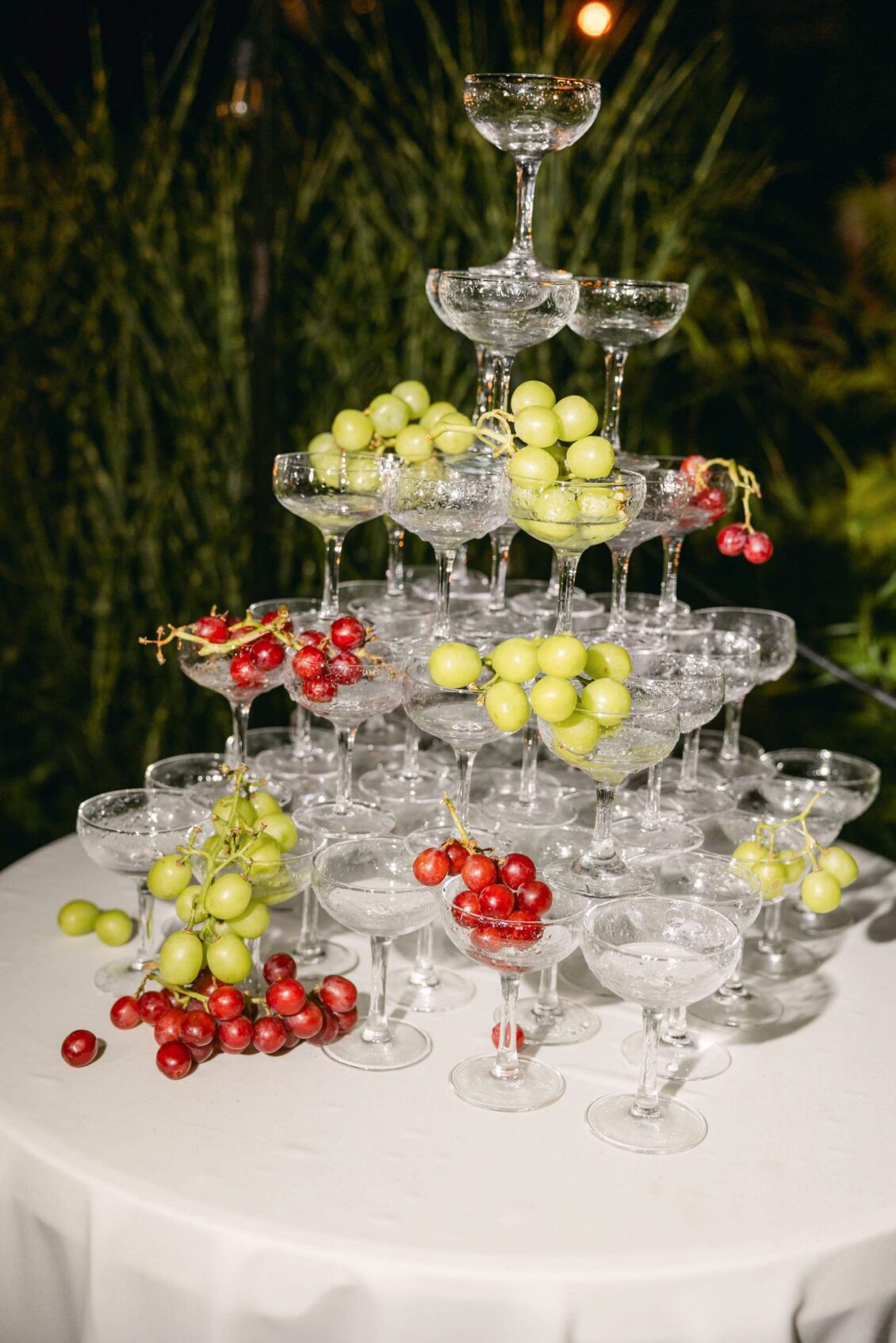 Champagne coupe tower dressed with red and green grapes on a round table