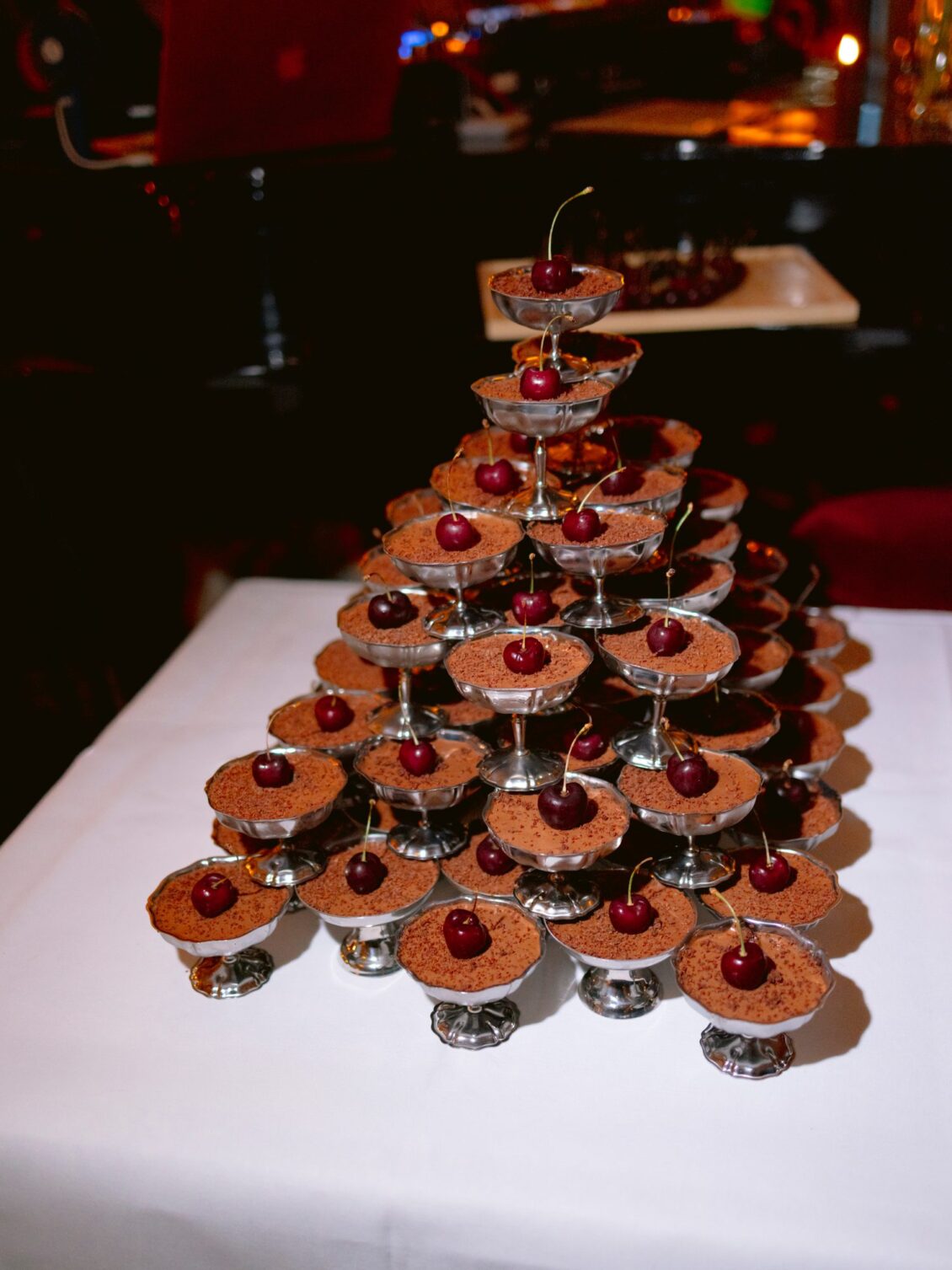 A tiered display of chocolate profiteroles topped with cherries on a white table
