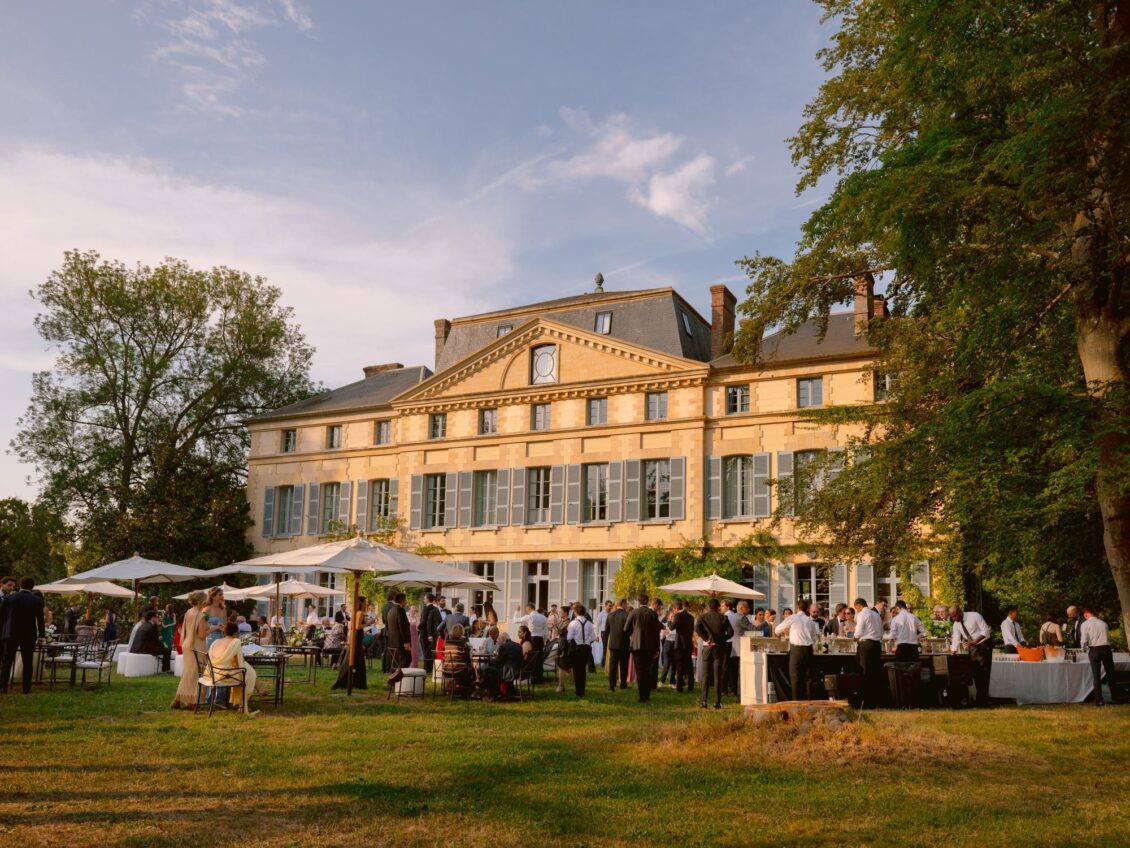 Guests mingle on the lawn under white parasols in front of the château at Domaine de Primard