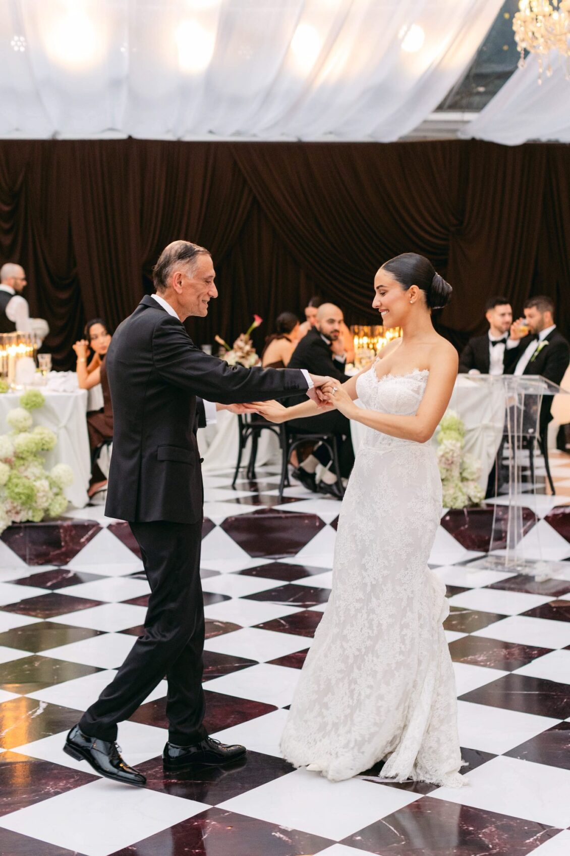 Lara and her father dance on a white and burgundy marble checkered floor