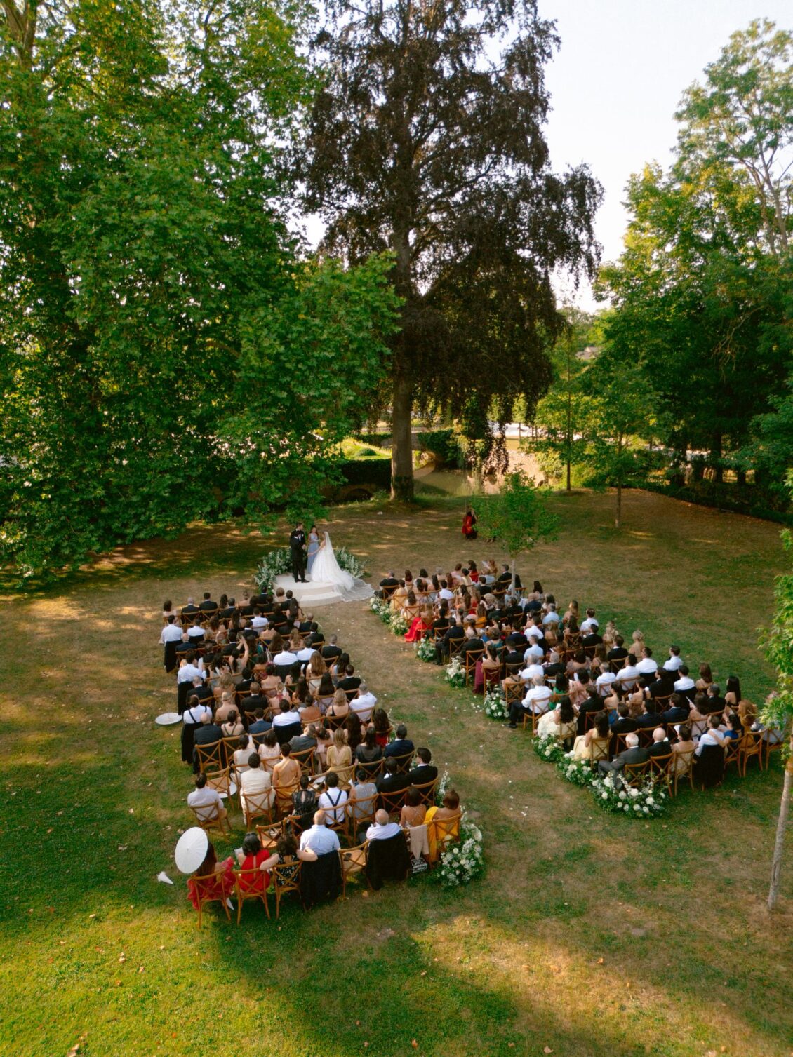 Elevated view of guests seated in the garden around the white ceremony platform beneath tall trees
