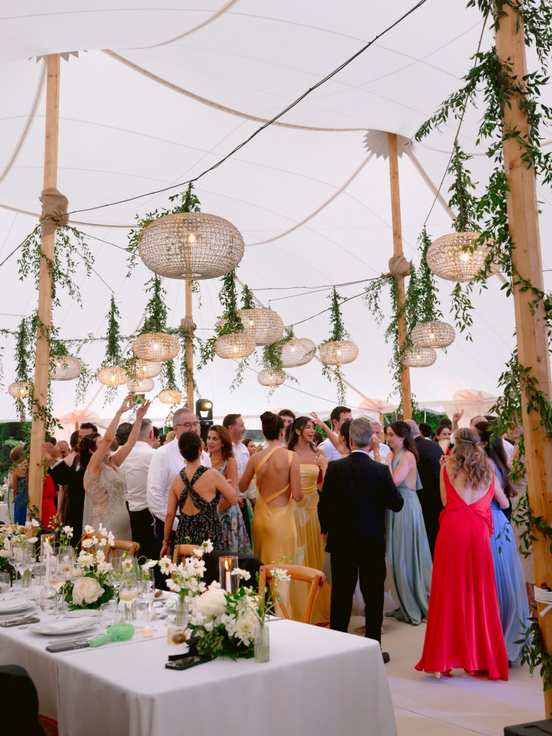Guests in colourful gowns raise their arms and cheer beside the reception tables
