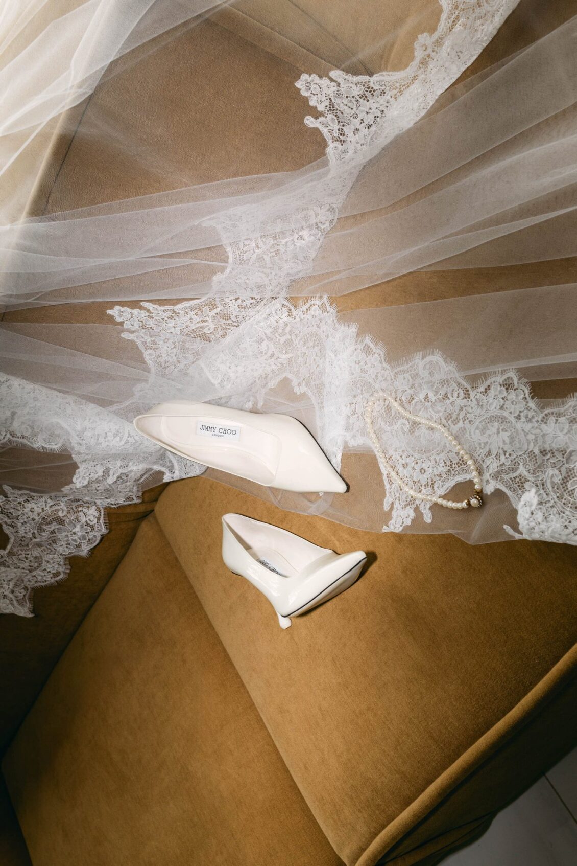 Lace-edged cathedral veil draped over a caramel chair with a pair of ivory pumps