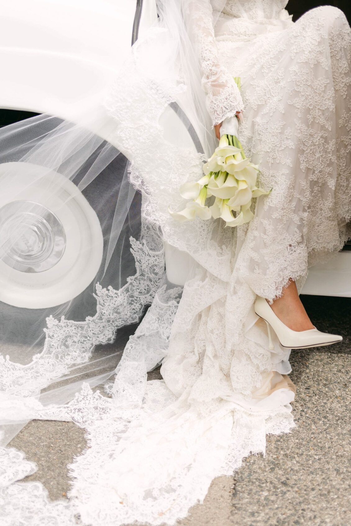Detail of Lara's lace veil, ivory pump and calla lily bouquet as she steps from a white vintage car