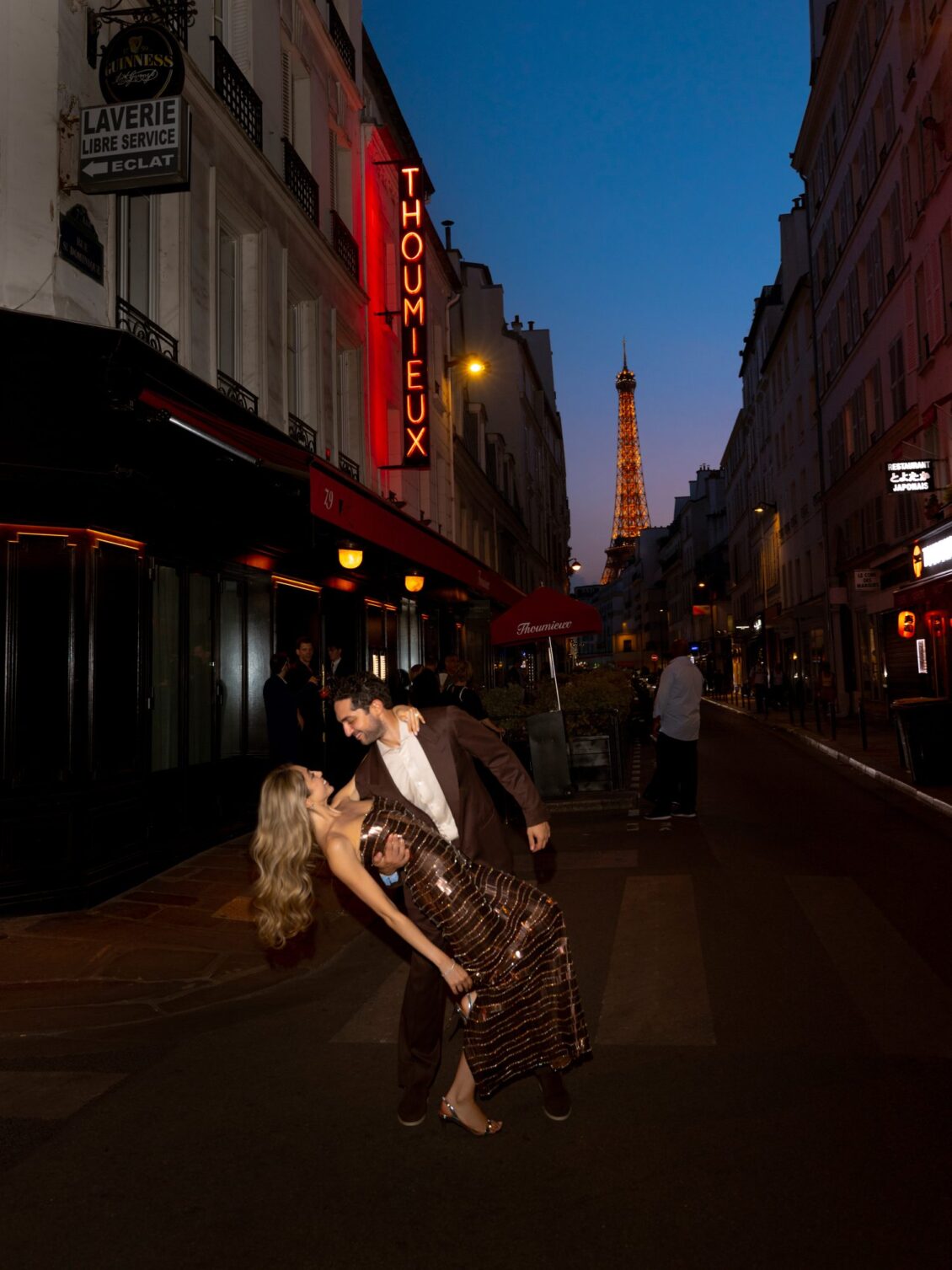 Sam dips Lamya on a Paris street outside Thoumieux with the lit Eiffel Tower in the distance