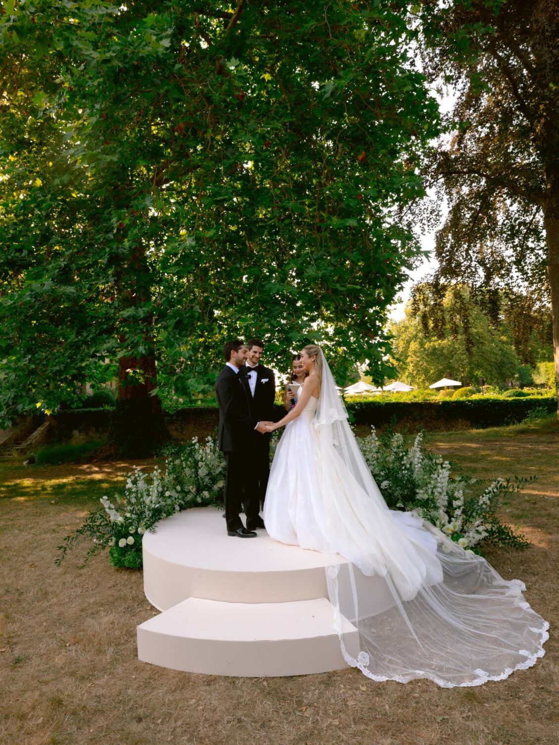Lamya and Sam face each other on the white platform as her veil cascades down the steps