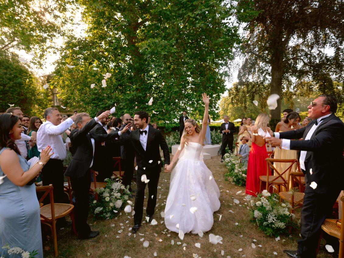 Lamya and Sam walk back up the aisle as cheering guests toss petals in the garden