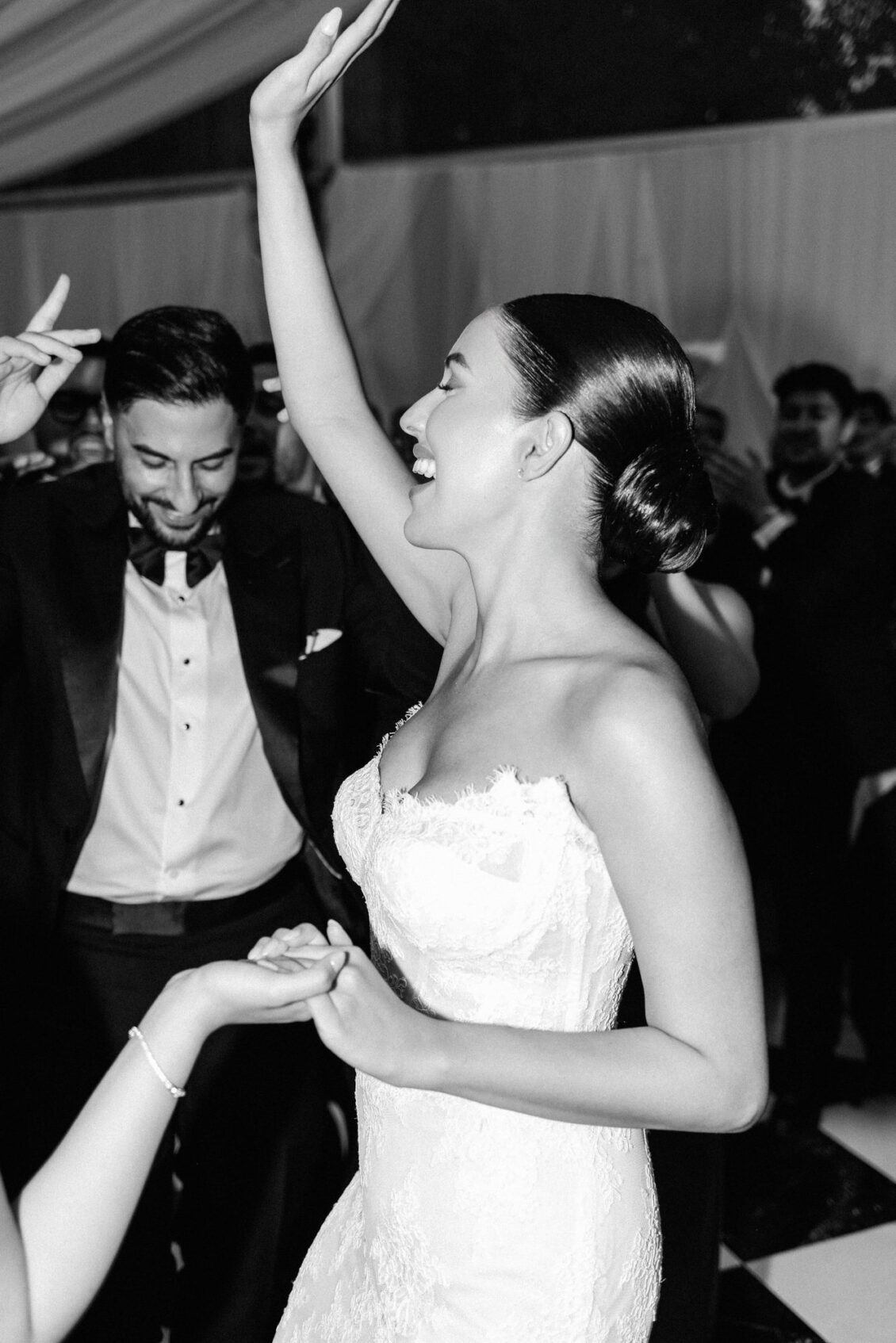 Black and white photo of Lara and Alex dancing with guests, Lara's arm raised