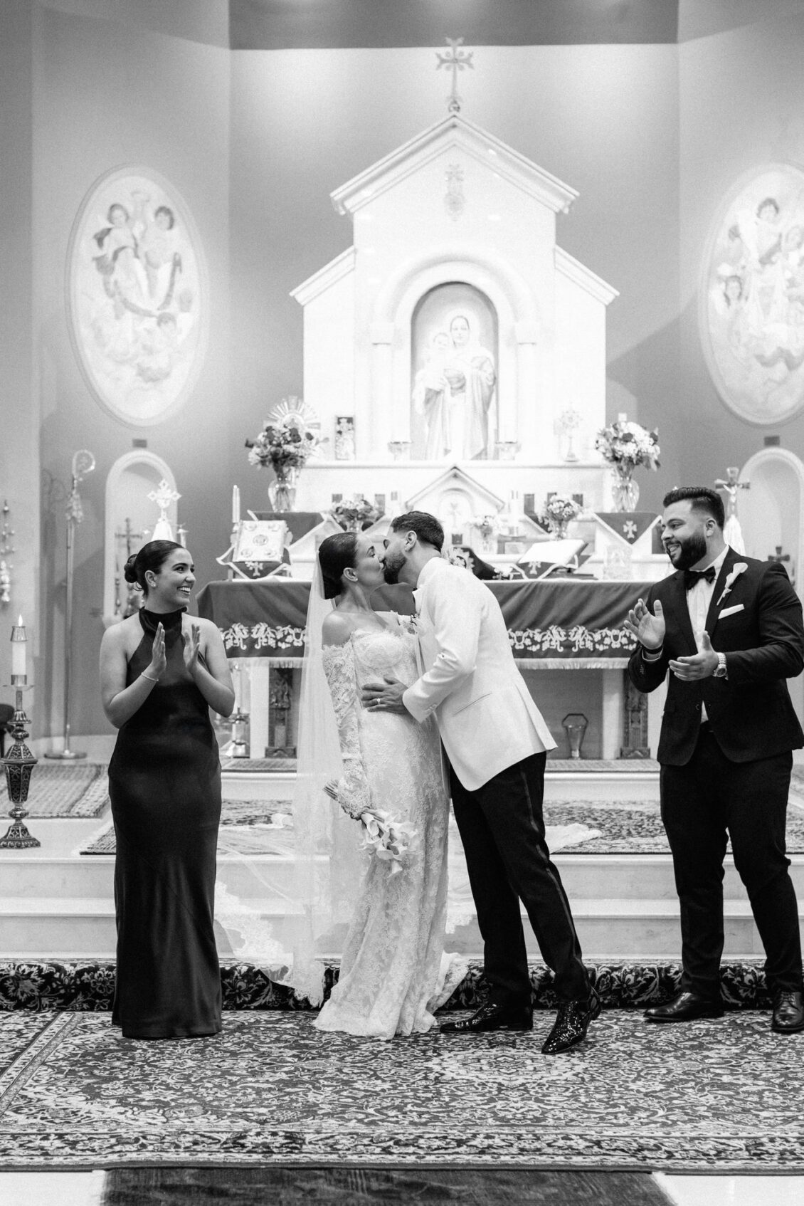 Black and white photo of Lara and Alex kissing at the altar beside their attendants