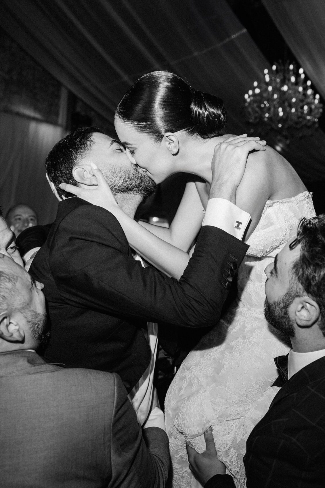 Black and white photo of Lara and Alex kissing as guests lift them on the dance floor
