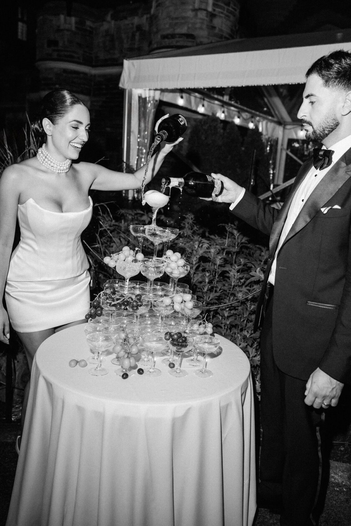 Black and white photo of Lara and Alex pouring champagne over the coupe tower