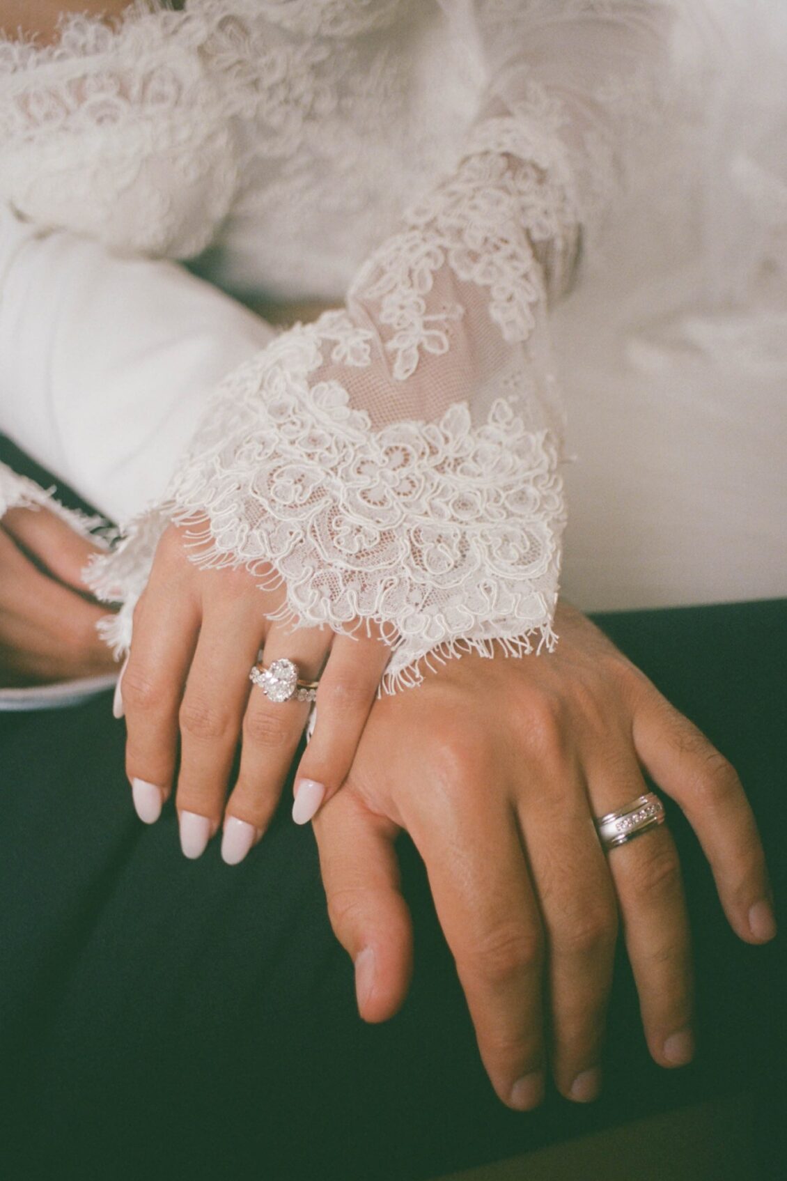 Close view of Lara's hand with her rings and lace cuff resting on Alex's hand with his wedding band