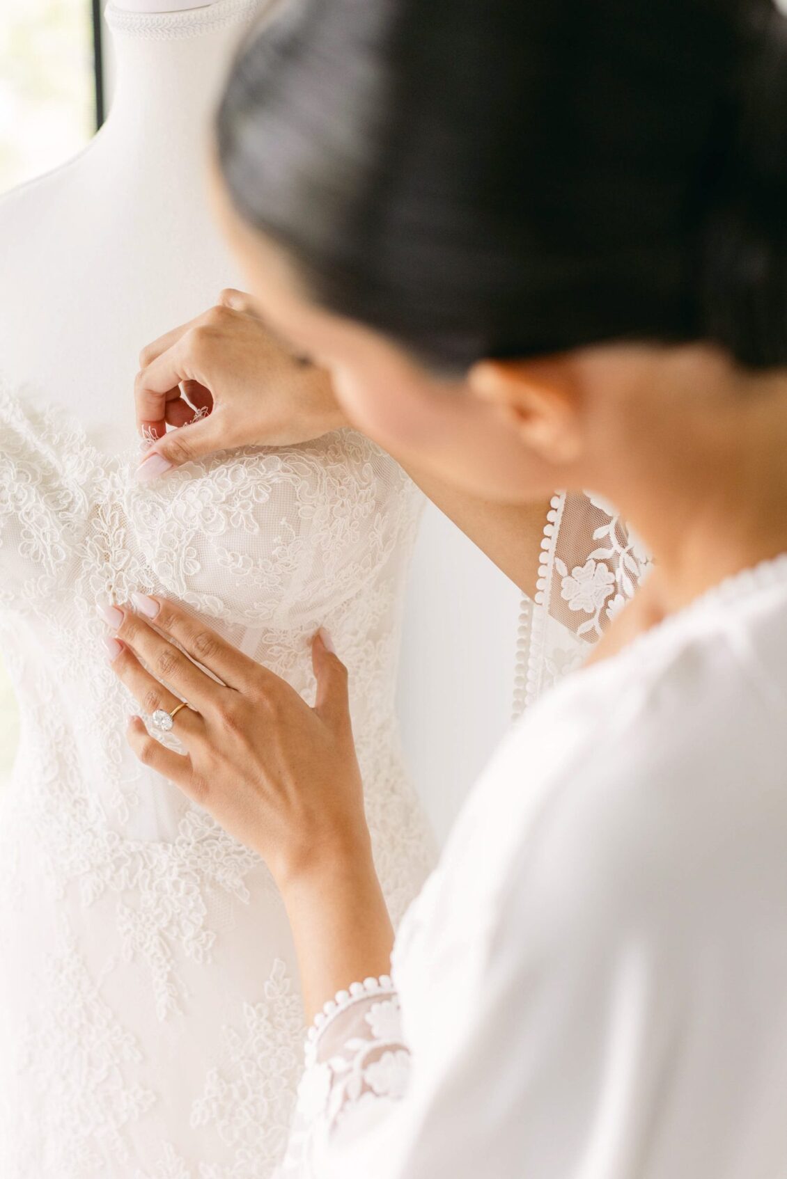 Close view of Lara's hand resting on the lace bodice of her wedding gown on a dress form