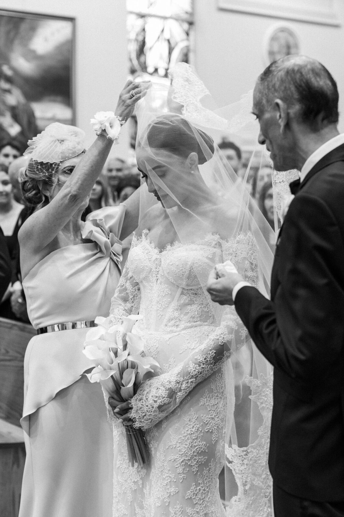 Black and white photo of a woman lifting Lara's veil at the front of the church as her father stands beside her