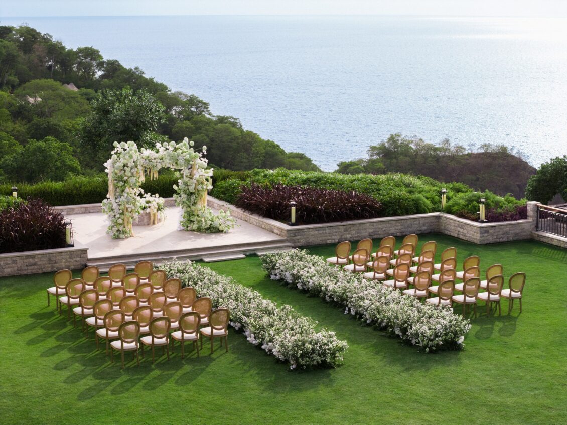 Open-air wedding ceremony beside a pool with white flowers and Pacific Ocean views at Nekajui