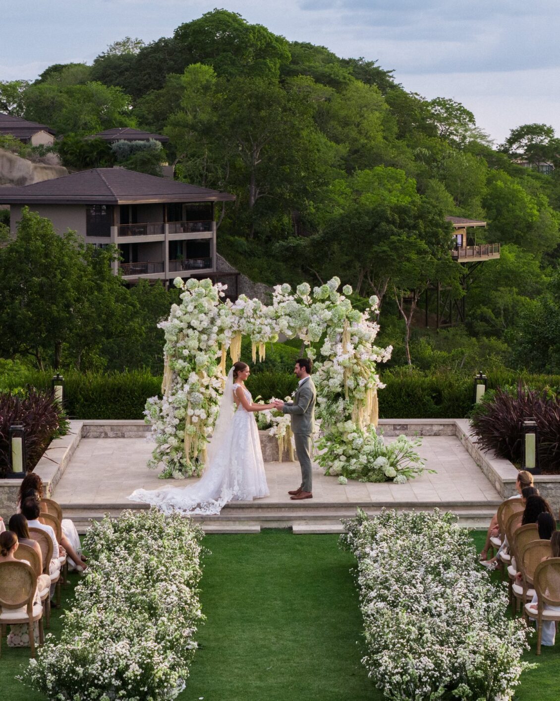 Bride and groom exchanging vows beneath a white floral ceremony arch at Nekajui, Costa Rica