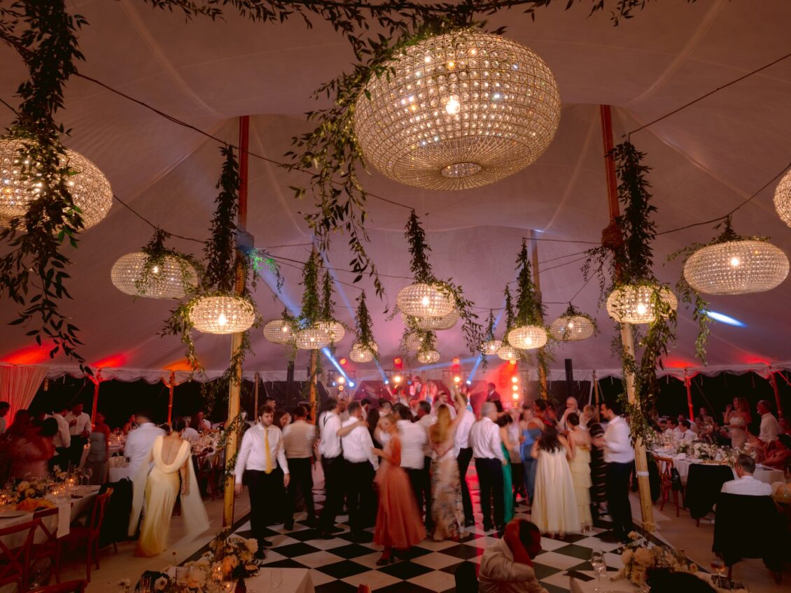 Guests fill the dance floor beneath crystal chandeliers and hanging greenery late in the evening