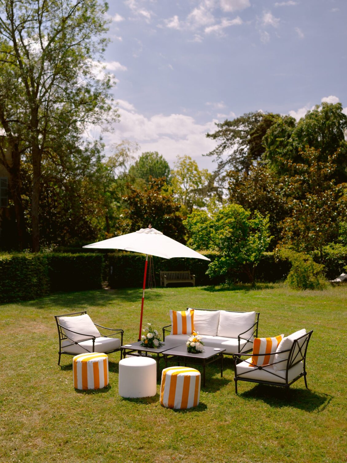 A white lounge set with yellow-and-white striped poufs beneath a parasol on the lawn