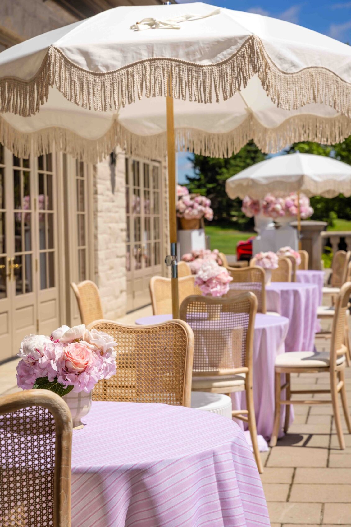 Lavender terrace tables arranged beneath fringed umbrellas