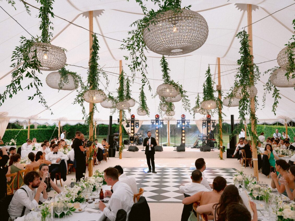 Guests at long tables watch a singer perform on the chequered dance floor in the tent