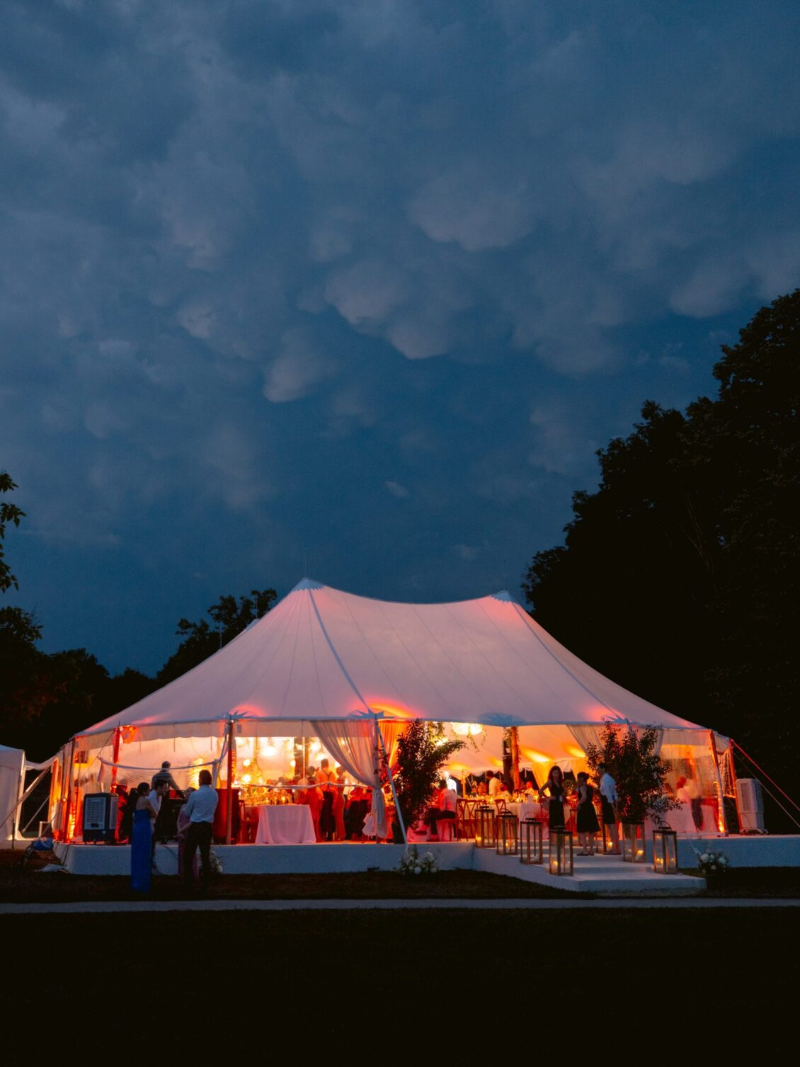 The white reception tent lit from within beneath a dramatic night sky