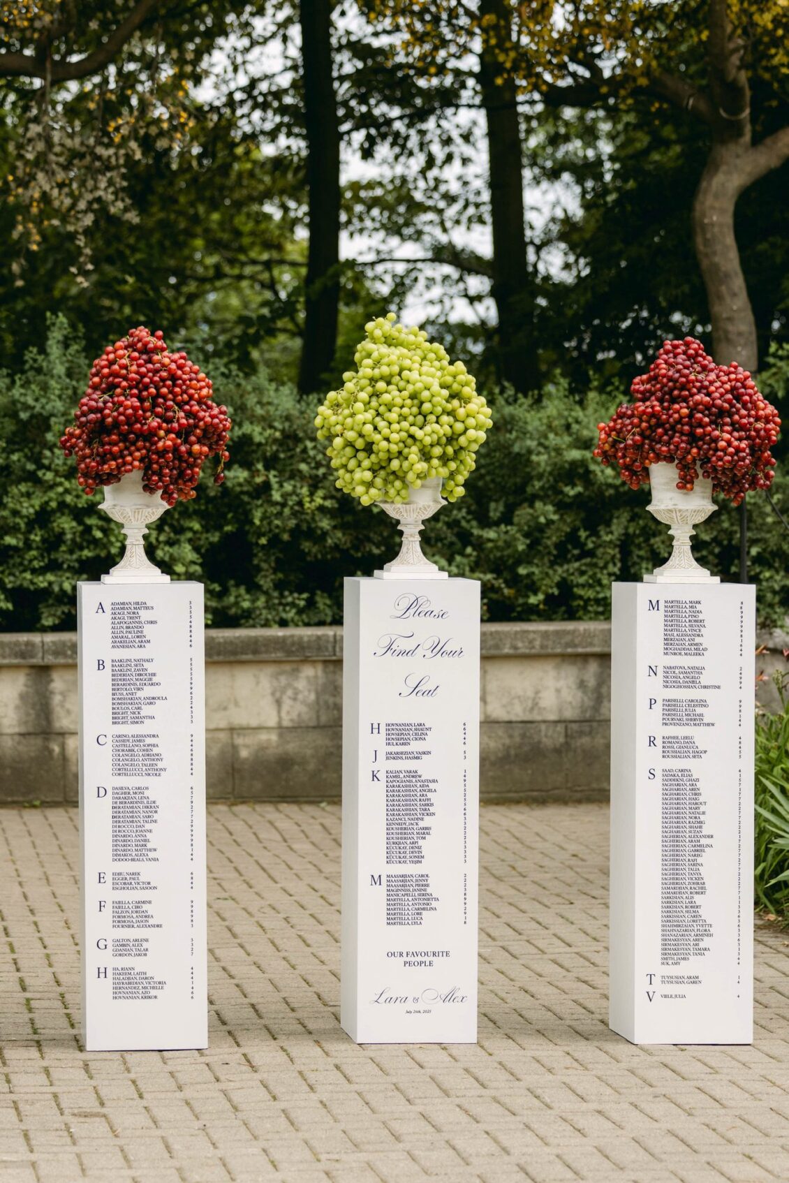 Three white pillars printed with the seating chart and topped with urns of red and green grapes