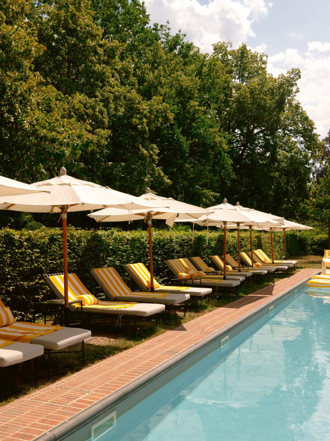 A row of loungers and white parasols lining the pool at Domaine de Primard
