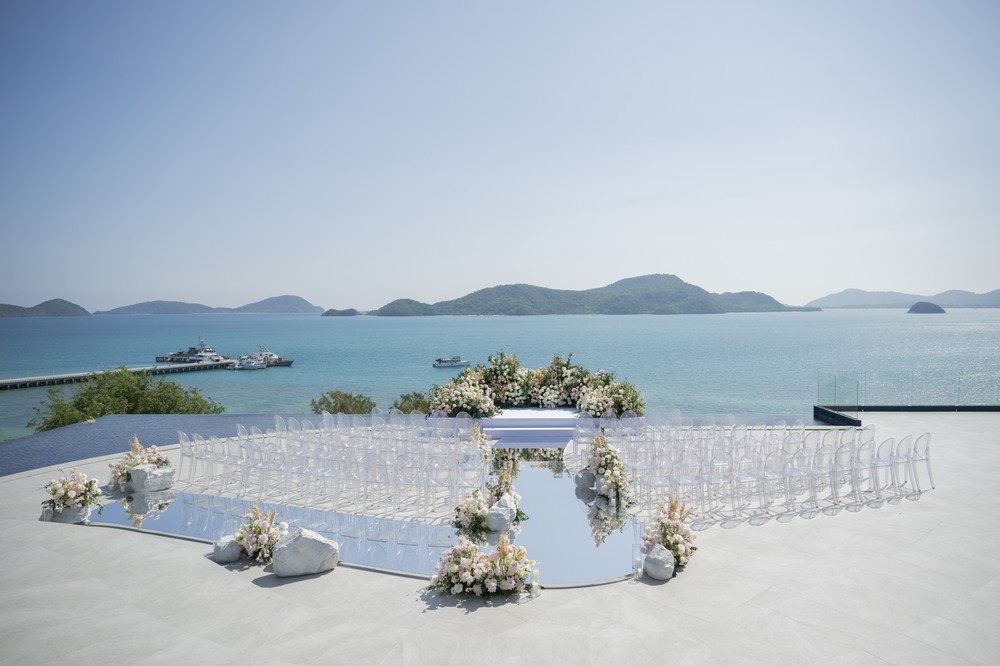 Vivian and Josen’s romantic destination wedding at Trisara Phuket — wide empty ceremony setting with mirrored aisle, flowers, and sea