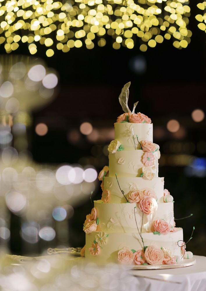 Vivian and Josen’s romantic destination wedding at Trisara Phuket — tiered floral wedding cake beneath blurred lights