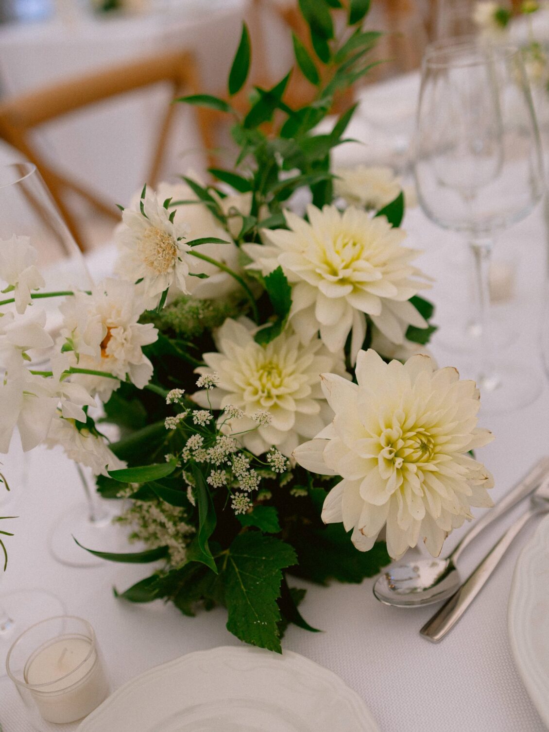 A centrepiece of white dahlias and garden greenery on a white reception table